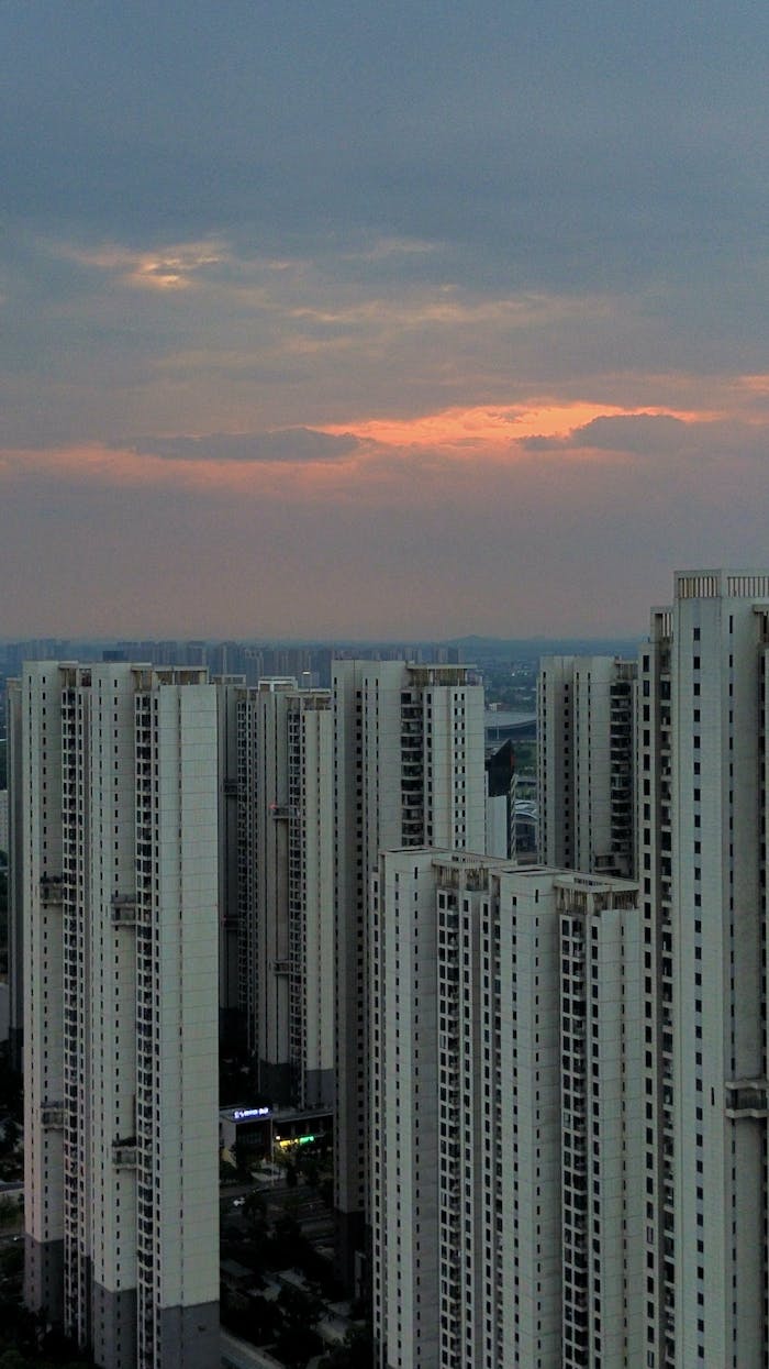 Home Tall skyscrapers under a dramatic sunset sky create an urban landscape scene.